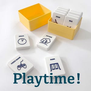 May include: A set of white rectangular activity tiles with dark blue icons and text including DRAW, BIKE, BREAK, OUTSIDE, VIDEO GAME, and PARK. The tiles are stored in two yellow plastic containers, with some tiles placed outside the boxes.