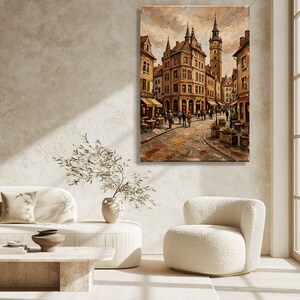 May include: A vertical oil painting on canvas depicting a European town square with multi-story buildings, a tall clock tower, and cobblestone streets. The scene features warm brown and orange tones with pedestrians walking near outdoor cafe tables.