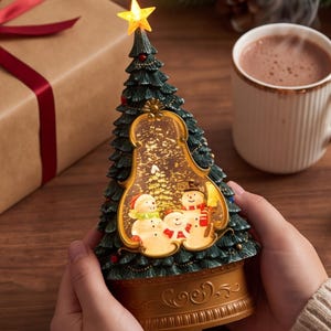 May include: A conical Christmas tree-shaped snow globe featuring a dark green textured exterior with red accents and a glowing yellow star topper. The center window displays three illuminated snowmen, while the base is a solid gold-colored pedestal.