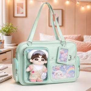 Peut inclure: Un sac fourre-tout vert menthe doté d'une poche frontale transparente contenant une poupée en peluche, une seconde poche transparente avec un motif arc-en-ciel et nuages, et une étiquette assortie avec un imprimé nuage, le tout avec des détails argentés.