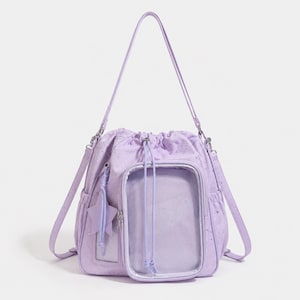 May include: A light purple drawstring backpack featuring a clear rectangular front pocket, silver star-shaped patterns across the fabric, a matching star-shaped charm attached to the side, and adjustable shoulder straps with silver hardware.