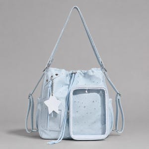 May include: A light blue backpack featuring a star pattern, a drawstring closure, and a clear rectangular front pocket. The bag includes adjustable shoulder straps, side pockets, and a white star-shaped charm attached to a silver chain.