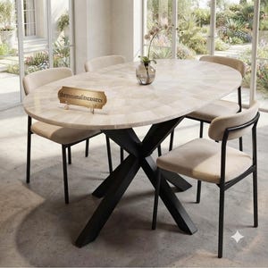 May include: An oval dining table with a light-coloured, tiled stone surface and a black metal X-shaped base, accompanied by four matching chairs with cream-coloured upholstered seats and black frames. A small sign reads theminimalitreasures.