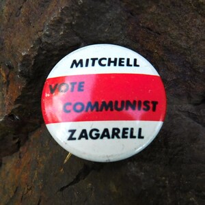 May include: A white button with red and black text that reads "Vote Mitchell Communist Zagarrell".