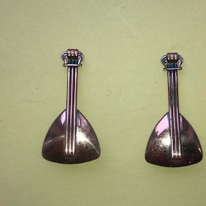 May include: A pair of gold-toned metal earrings shaped like a lute or mandolin. The earrings are about 2 inches long and have a detailed design.