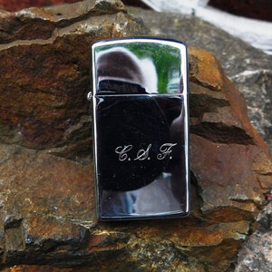 May include: A silver lighter with a black finish and the initials "C.S.F." engraved on the front.