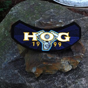May include: A blue and yellow embroidered patch with the word "HOG" and the years "1999" on a rock.
