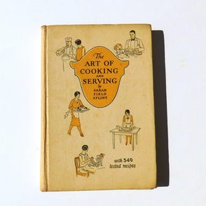 Puede incluir: La portada de un libro de cocina vintage titulado "The Art of Cooking and Serving" de Sarah Field Splint. La portada presenta ilustraciones de personas cocinando y sirviendo comida, y el texto "with 549 tested recipes".
