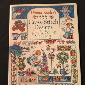 May include: A book titled "Donna Kooler's 555 Cross-Stitch Designs for the Young at Heart" with a colorful cover featuring various cross-stitch designs.