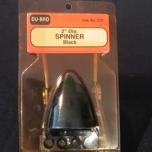 May include: A black 2-inch diameter spinner for model airplanes, packaged in a clear plastic bag with the brand name "DU-BRO" and the product name "SPINNER Black" printed on the label. Cat. No. 273 is also printed on the label.