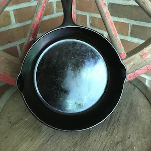 May include: A black cast iron skillet with a loop handle. The skillet is sitting on a wooden surface.