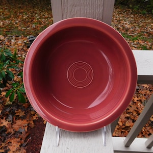 May include: A deep red ceramic bowl with a smooth, glossy finish. The bowl has a simple, circular design with concentric circles in the center.