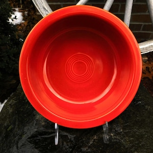 May include: A bright red ceramic bowl with a circular design in the center. The bowl is sitting on a dark gray surface.