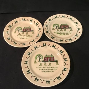 Peut inclure: Ensemble de trois assiettes à dessert en céramique de couleur crème avec une bordure verte et rouge. Chaque assiette présente une illustration peinte à la main d'une maison rouge avec un toit vert, un arbre vert et des balles de foin.