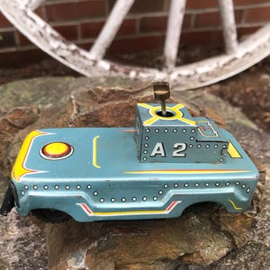 May include: A vintage teal toy car with yellow and red detailing. The toy car has the number "A 2" and a wind-up key. The car is made of metal and has a retro design, ideal for collectors.