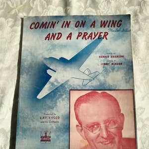 May include: A vintage sheet music cover for the song "Comin' In On A Wing And A Prayer" by Harold Adamson and Jimmy McHugh. The cover features a black and white illustration of an aeroplane and a photo of Kay Kyser, the song's performer.