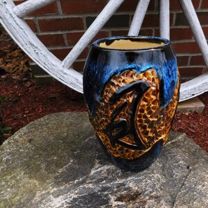 May include: A blue and gold ceramic vase with a textured surface. The vase has a unique design with a stylized letter Z.