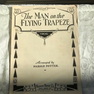 May include: A vintage sheet music cover for a song titled "The Man on the Flying Trapeze". The cover features a decorative border with hearts and a banner that reads "Vocal". The music is arranged by Harold Potter and published by Morris Music Co. in Philadelphia, PA.