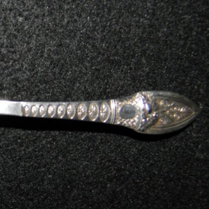 May include: A silver spoon with an ornate handle. The spoon has a rounded bowl and a long, slender handle with a decorative design.