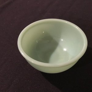 Op de afbeelding: Een kleine, ronde, lichtgroene kom met een gladde, glanzende afwerking. De kom heeft een eenvoudig, klassiek ontwerp en is waarschijnlijk gemaakt van keramiek of glas. Het is geschikt voor het serveren van kleine porties voedsel of als decoratief item.