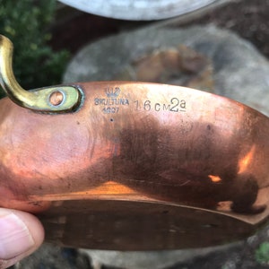 Op de afbeelding: Een koperen kookpan met een messing handvat. De pan is gemarkeerd met de tekst "SKULTUNA 1607" en "1.6 CM2a".