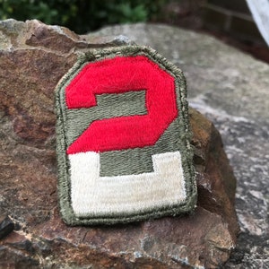 Puede incluir: Un parche bordado verde, blanco y rojo con el número "2" en un círculo rojo.