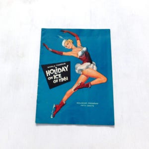 Könnte beinhalten: Ein Vintage-Souvenirprogramm für "Holiday on Ice" aus dem Jahr 1961. Das Cover zeigt eine Frau in einem rot-weißen Kostüm, die auf einem blauen Hintergrund Schlittschuh läuft. Der Text "World Famous Holiday on Ice of 1961" ist in Schwarz gedruckt. Das Programm kostet fünfzig Cent.