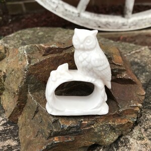 May include: White ceramic owl napkin ring. The owl is perched on a branch with leaves. The ring is designed to hold a napkin.