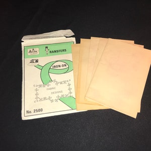 Puede incluir: Un paquete de diseños de transferencia de tela para planchar. El paquete es blanco con detalles en verde y negro. El paquete dice "Transfers Iron-On Fabric Designs No. 2500".