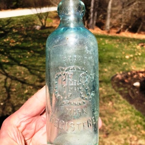 May include: A clear glass bottle with a rounded top and a textured surface. The bottle has a raised design with the text "TRADE MARK REGISTERED" and a circular design with the letters "C.G.S."