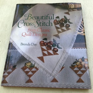 May include: A book titled "Beautiful Cross Stitch from Classic Quilt Designs" by Brenda Day. The cover features a white fabric with a cross-stitch design of a basket of fruit.