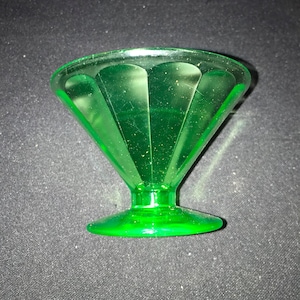 May include: A vintage green glass dessert dish with a flared, faceted bowl and a circular base. The dish has a stem and a vibrant, translucent green color, likely from the mid-20th century. The dish is designed for serving desserts.