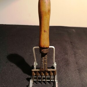 May include: A vintage ice pick with a wooden handle and metal prongs. The ice pick is labeled "Hamilton Beach No 50".