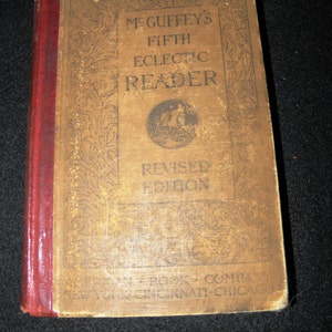 Op de afbeelding: Een vintage boek getiteld "McGuffey's Fifth Eclectic Reader, Revised Edition" met een rode rug en een sierlijk bloemmotief op de omslag. Het boek is uitgegeven door de American Book Company in New York, Cincinnati en Chicago.