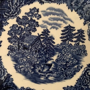 Puede incluir: Plato de porcelana azul y blanco con una escena de cabaña. La escena representa una cabaña pequeña, árboles y un río. El plato tiene un borde floral.