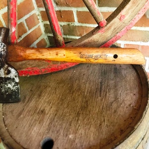 May include: A vintage wooden-handled axe with a metal head, resting on a wooden barrel. The handle is labeled "GENUINE HICKORY".