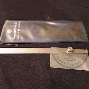 May include: A silver protractor with a black knob and a silver ruler attached. The protractor is labeled "GENERAL" and "MADE IN U.S.A.". The ruler is labeled "ESCO TOOL ROOM".