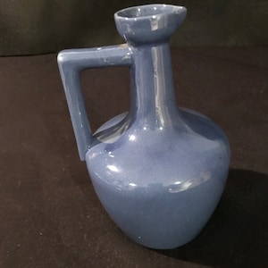 May include: A blue ceramic pitcher with a wide mouth and a handle. The pitcher has a smooth, glossy finish.