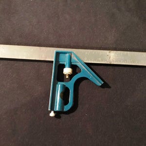 May include: A blue metal try square with a silver ruler. The ruler has markings in inches.