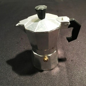 May include: A silver aluminium stovetop espresso maker with a black plastic handle and lid.