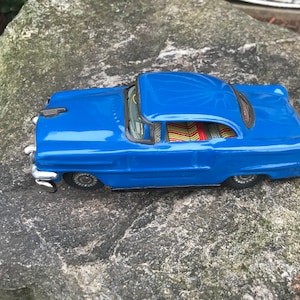 May include: A blue toy car with a black grill and chrome wheels. The car has a red and yellow striped interior.