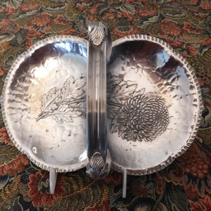 May include: A silver serving tray with two divided sections, each featuring an embossed floral design. The tray has a handle with decorative floral accents.