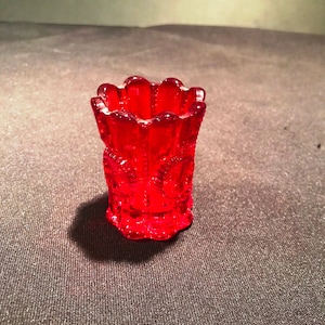 Op de afbeelding: Een kleine, rode glazen vaas met een getextureerd stervormig patroon. De vaas is ongeveer 5 cm hoog en heeft een gegolfde rand.