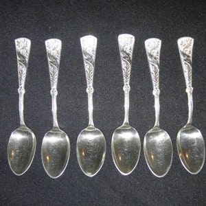 Puede incluir: Conjunto de siete cucharaditas de plata con mangos adornados. Las cucharas tienen un acabado pulido y están dispuestas en fila.