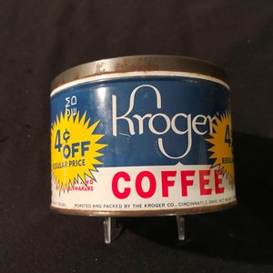 Op de afbeelding: Een vintage blauwe en gele Kroger koffieblik met een 4¢ korting. Het blik heeft een wit etiket met de tekst "Kroger Coffee" en "Roasted and Packed by the Kroger Co., Cincinnati 2, Ohio, Net Wt. 1 Pound."