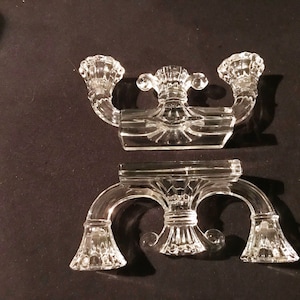 Peut inclure: Un ensemble de deux bougeoirs en verre transparent avec un design décoratif. Les bougeoirs sont en deux parties, la partie supérieure comportant trois bras incurvés et la partie inférieure comportant trois bras incurvés avec des cloches aux extrémités.
