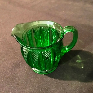 May include: A small, green glass creamer with a diamond pattern and a handle.