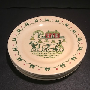 Peut inclure: Une pile de quatre assiettes plates de couleur crème avec une bordure verte et rouge. Le centre de l'assiette représente une scène de ferme avec une maison rouge, un arbre vert, deux chevaux tirant une charrue et un fermier.
