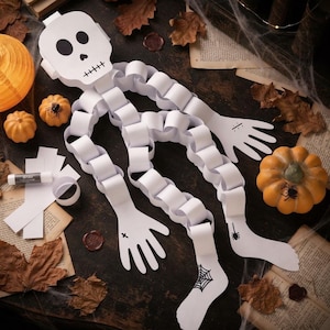 May include: A white paper chain skeleton craft featuring a skull head, linked paper limbs, and hand and foot cutouts with black ink illustrations of a spider, a spiderweb, and a cross. The skeleton is constructed from white paper strips.