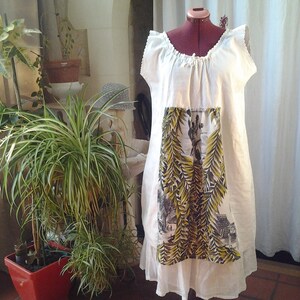 May include: A white linen dress with a floral print panel. The dress has a gathered neckline and a loose, flowing silhouette.